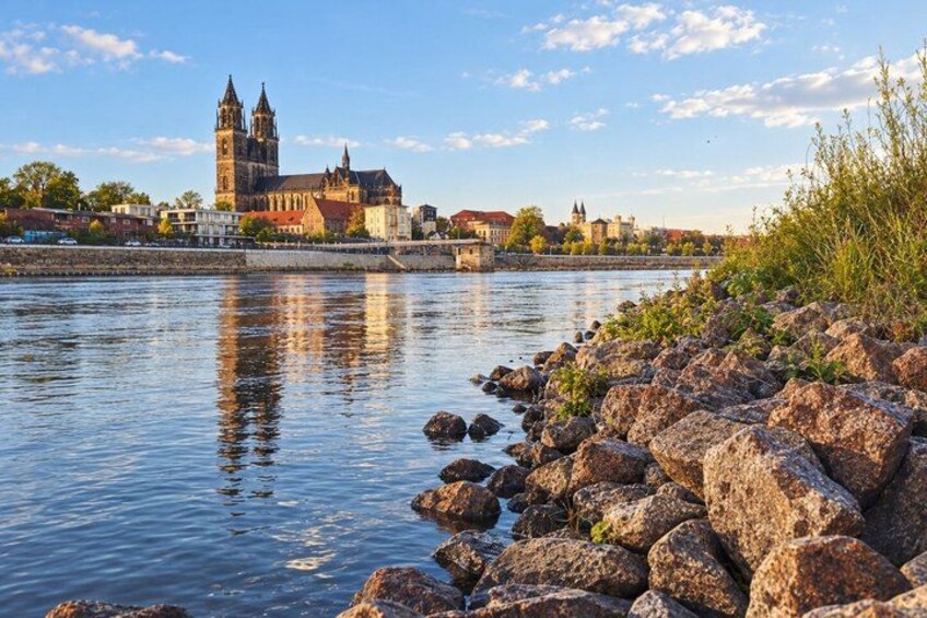 A river with a rocky shore, a bridge, and a historic building with towers in the background. 5
