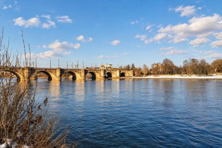 A stone bridge over a river with clear blue water, surrounded by trees and a clear sky. 2