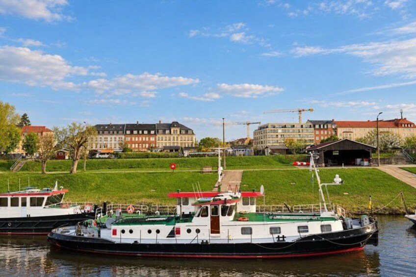 A river with boats, a grassy area, and buildings in the background. 5