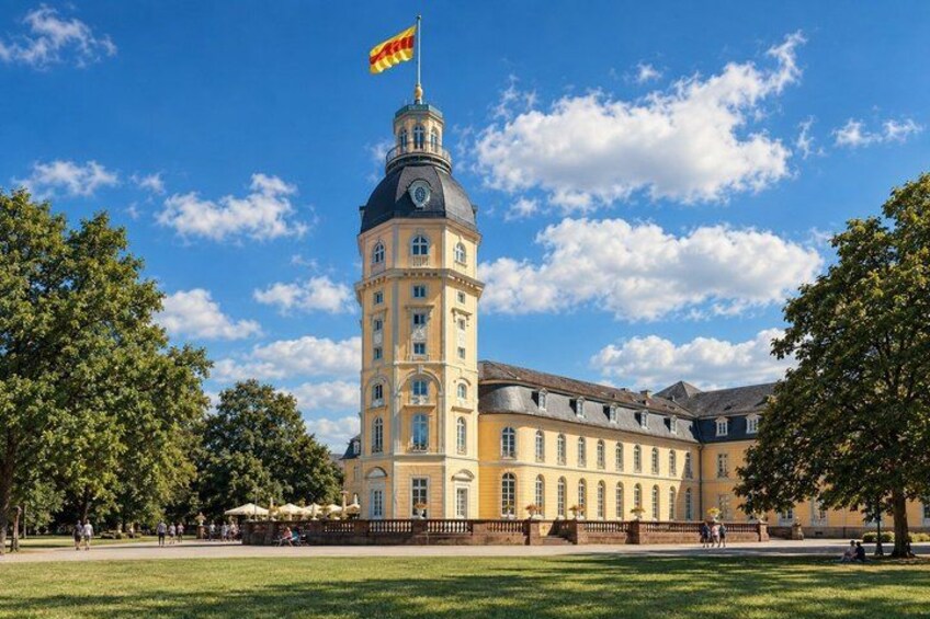 A historic building with a tower, surrounded by a park with trees and a clear sky. 3