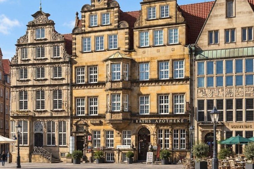 A historic building with ornate architecture, a sign for 'Raths Apotheke', and outdoor seating. 3