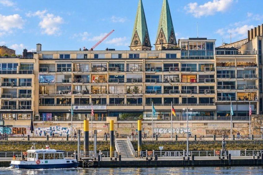 A waterfront building with two spires, a dock with a boat, and a pedestrian walkway. 2