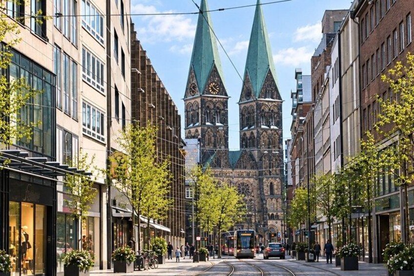 A street with buildings, a tram, and a church with two spires. 5
