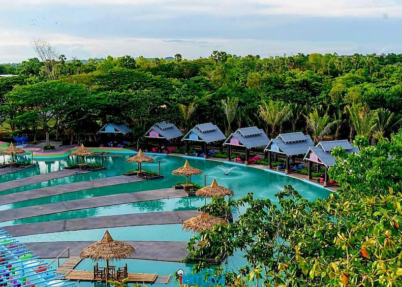 A tropical resort with a large swimming pool, thatched-roof huts, and lush greenery. 1