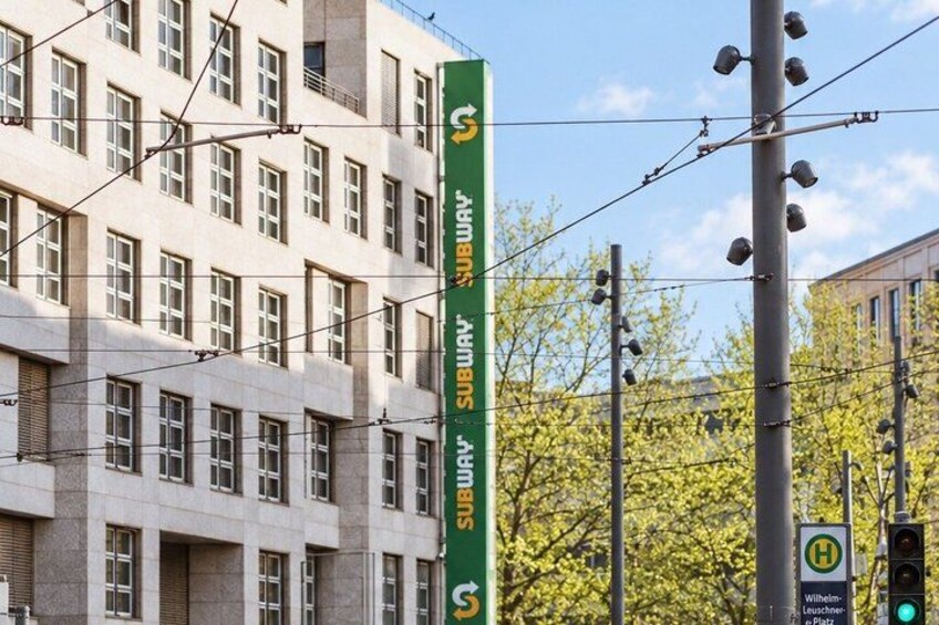 A green subway sign, a building with multiple windows, and a traffic light. 3