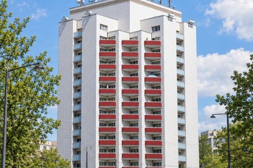 A multi-story residential building with balconies, surrounded by trees and a clear sky. 2