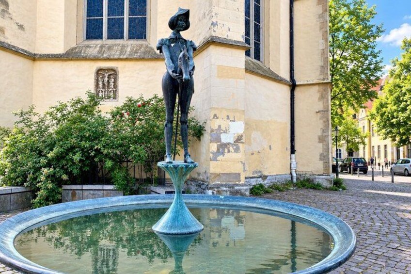 A statue of a woman on a pedestal in front of a building with a window and a tree. 4
