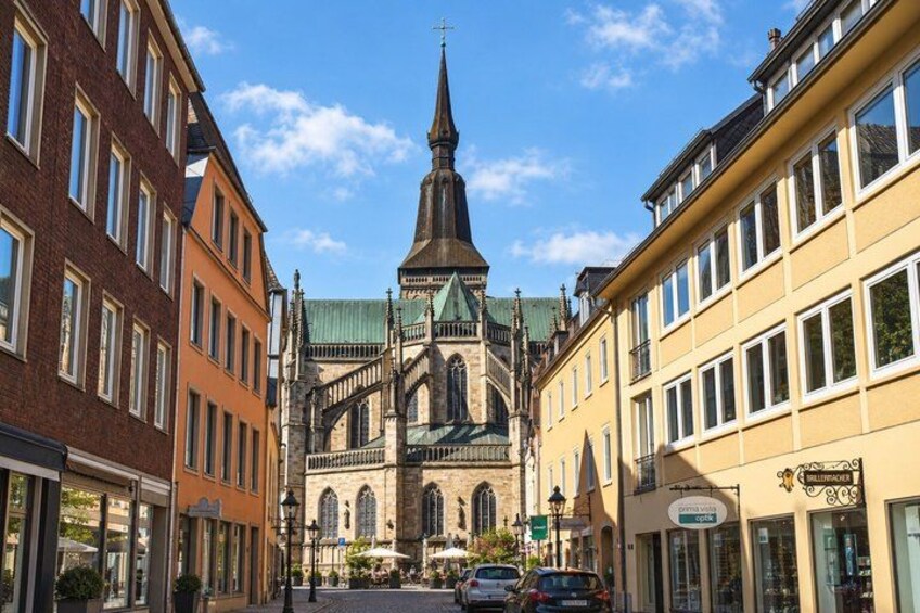A church with a tall spire, surrounded by buildings with large windows and a clear blue sky. 2