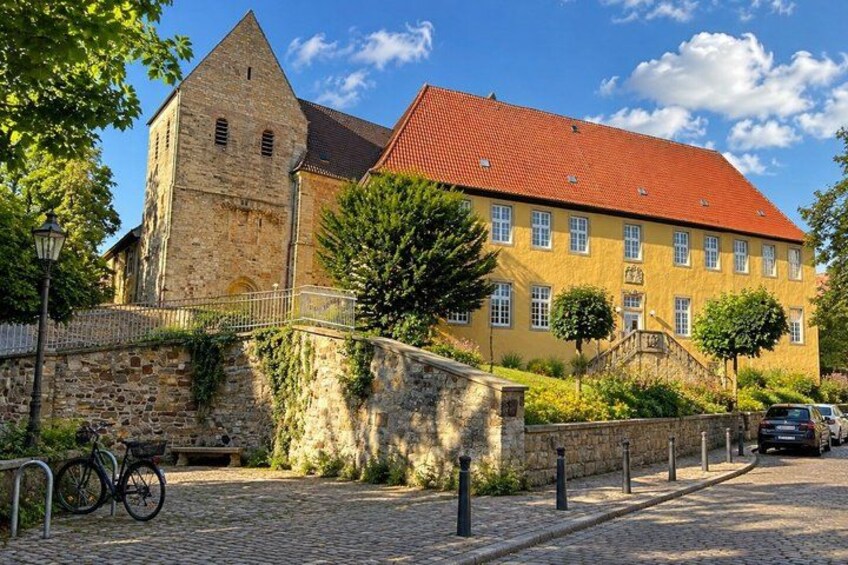 A historic building with a red roof, a stone tower, and a paved street with a bicycle. 2