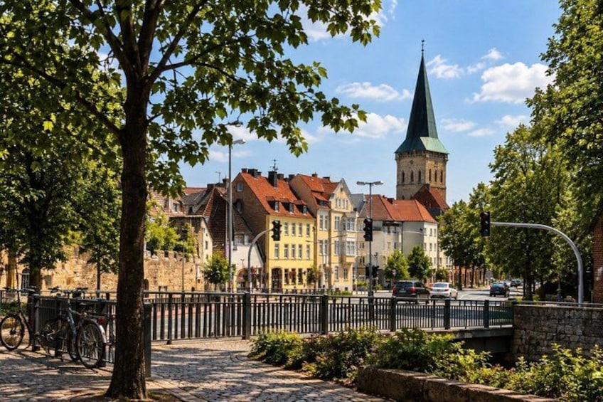 A cobblestone street lined with trees, historic buildings, and a church tower. 4