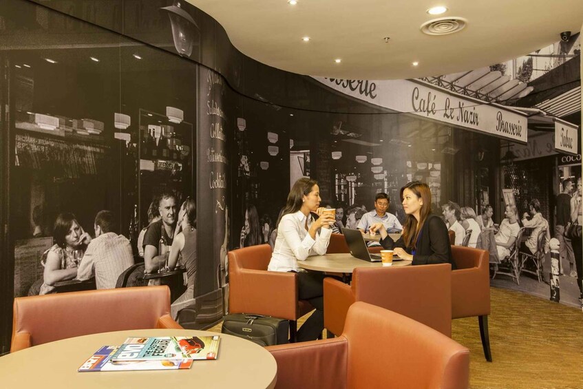 A cafe interior with round tables and orange chairs, featuring a wall with black and white photographs and text. 3