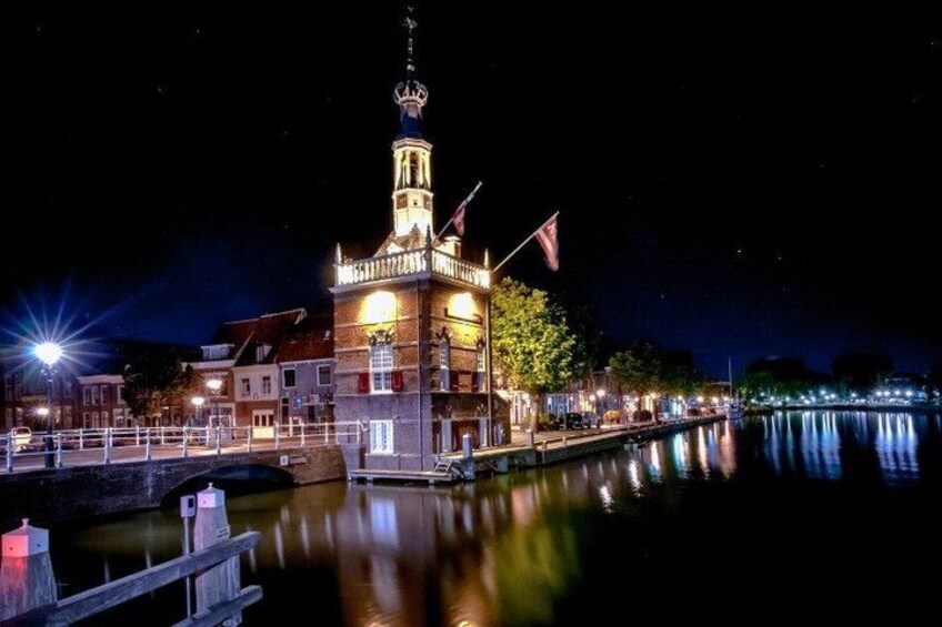 A lit-up building with a tower, a calm water body in the foreground, and a dock with a railing. 5