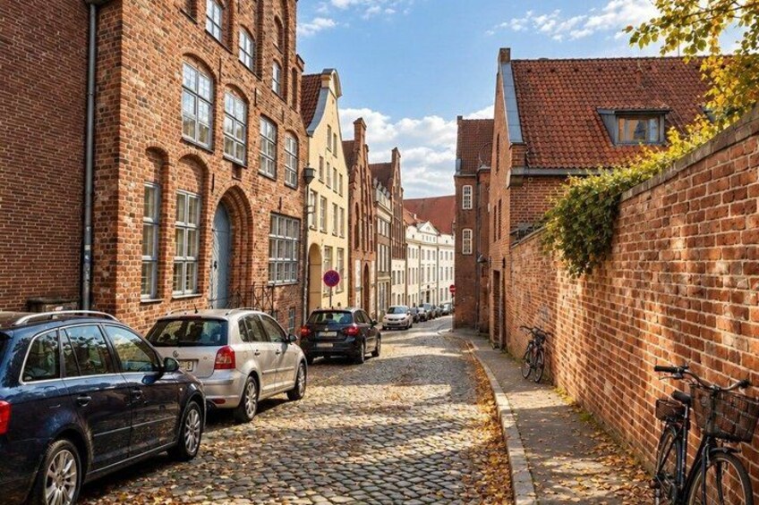 A cobblestone street lined with brick buildings, parked cars, and a bicycle. 3