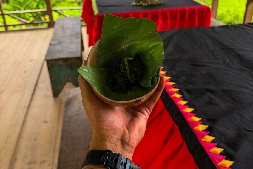 A hand holding a wooden bowl with a food item wrapped in banana leaves. 2