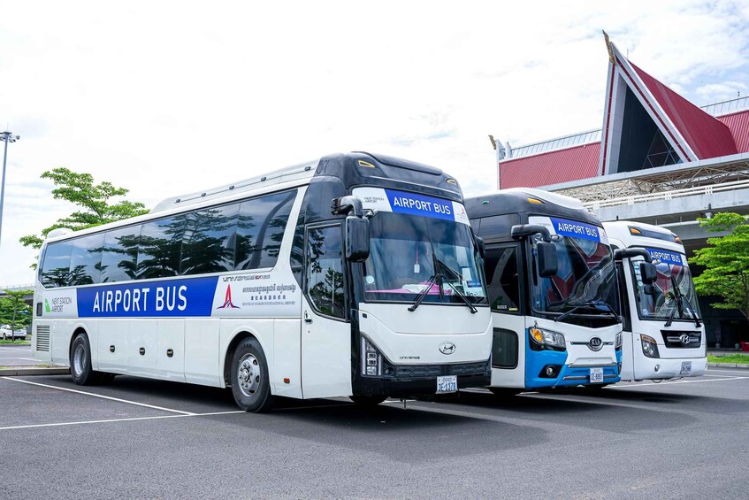 Two airport buses parked in a lot with a building in the background. 1