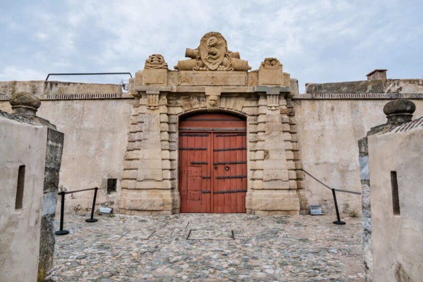 A stone building with a large red door, a lion sculpture above the door, and a cobblestone path leading to the entrance. 4