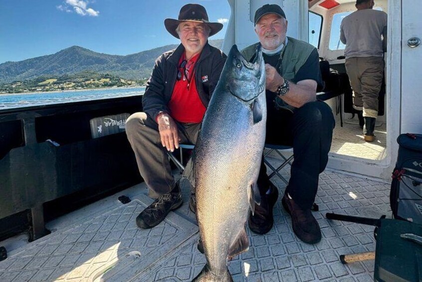 Two men on a boat holding a large fish. 1