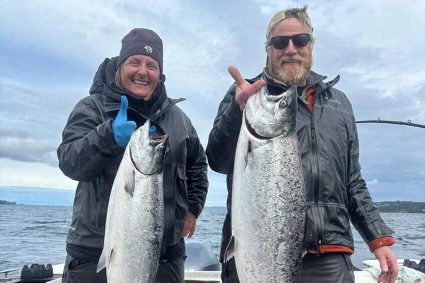 Two people holding large fish on a boat with a cloudy sky in the background. 4