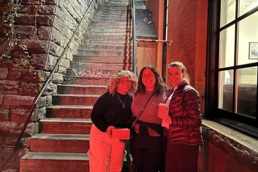 Three people standing on a staircase next to a brick building with a window. 3