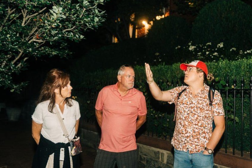 Three people standing outdoors at night, with a tree and a fence in the background. 1