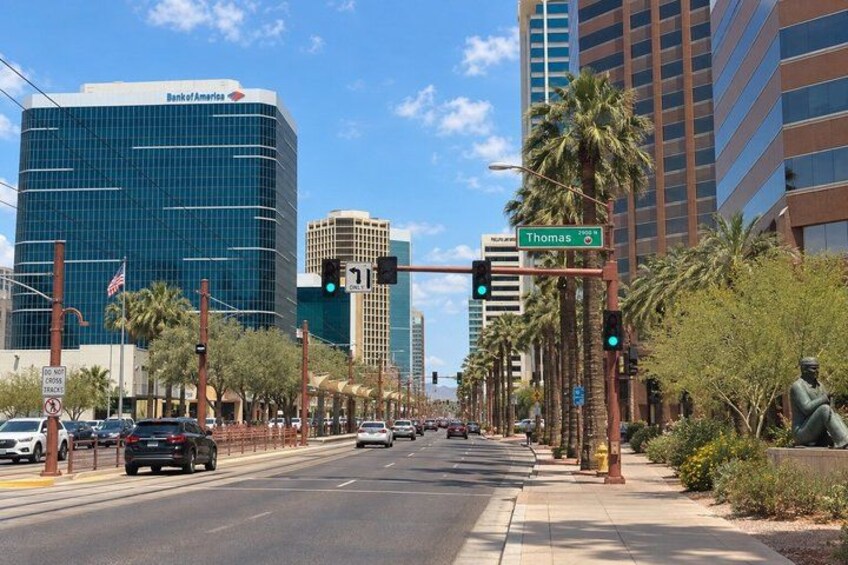 A city street with traffic lights, palm trees, and modern buildings including a Bank of America skyscraper. 2