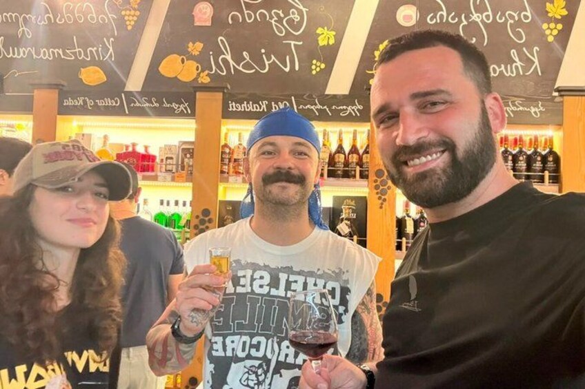 A person holding a glass of red wine, a bar with shelves of bottles, and a chalkboard with writing. 1