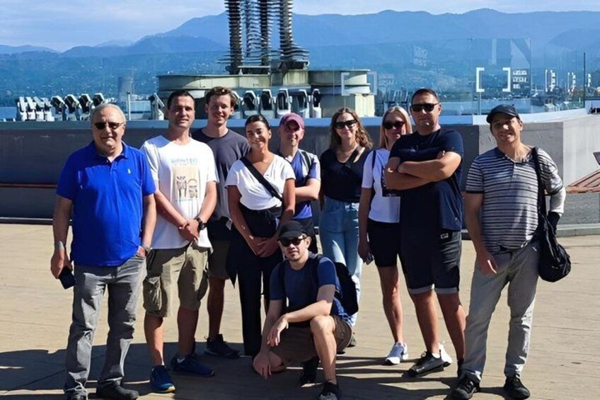 A group of people standing in front of a large ship with mountains in the background. 3