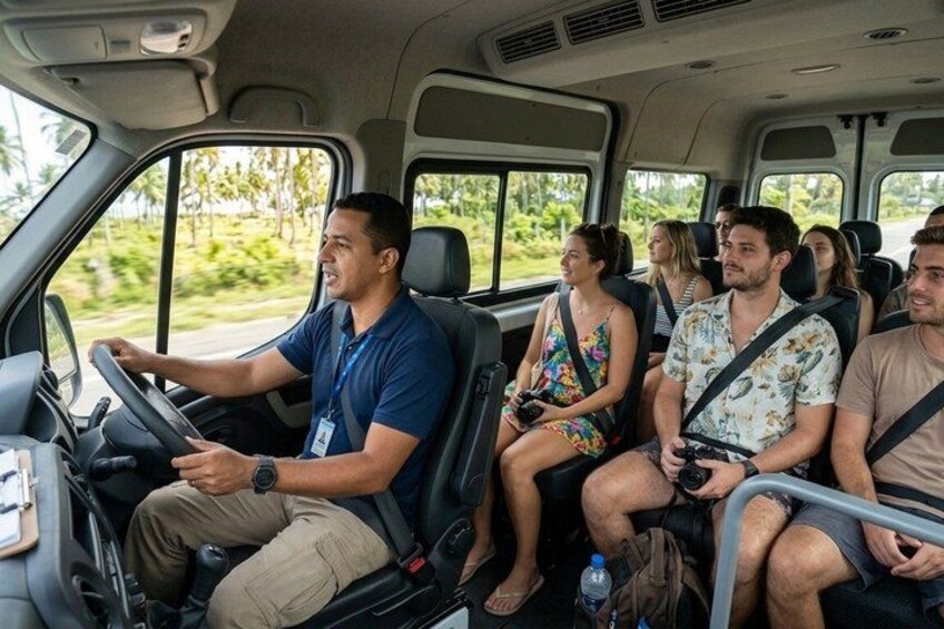 A vehicle interior with passengers, a steering wheel, and a window showing greenery outside. 5