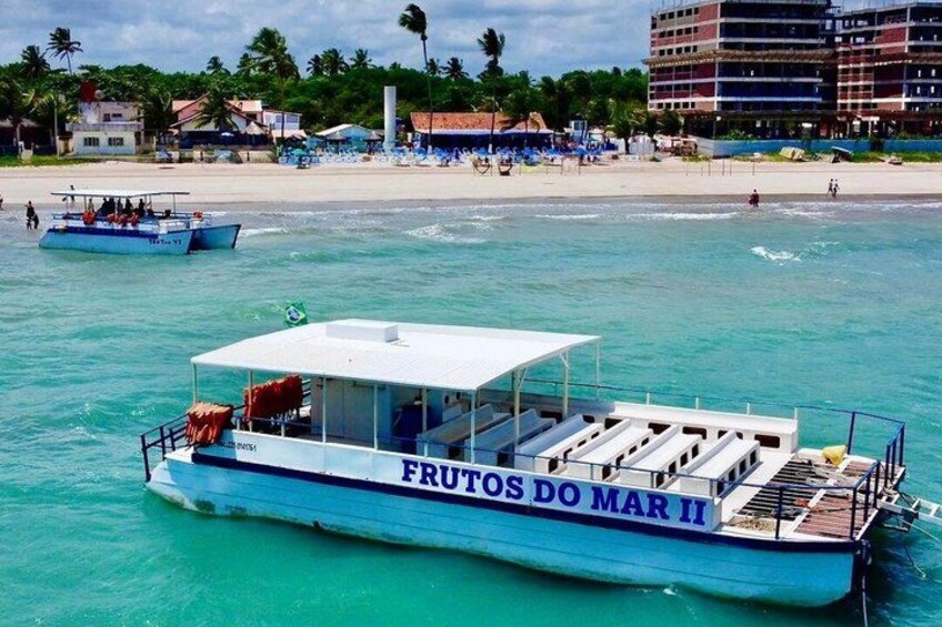 A boat named FRUTOS DO MAR II on turquoise waters with a beach and buildings in the background. 2