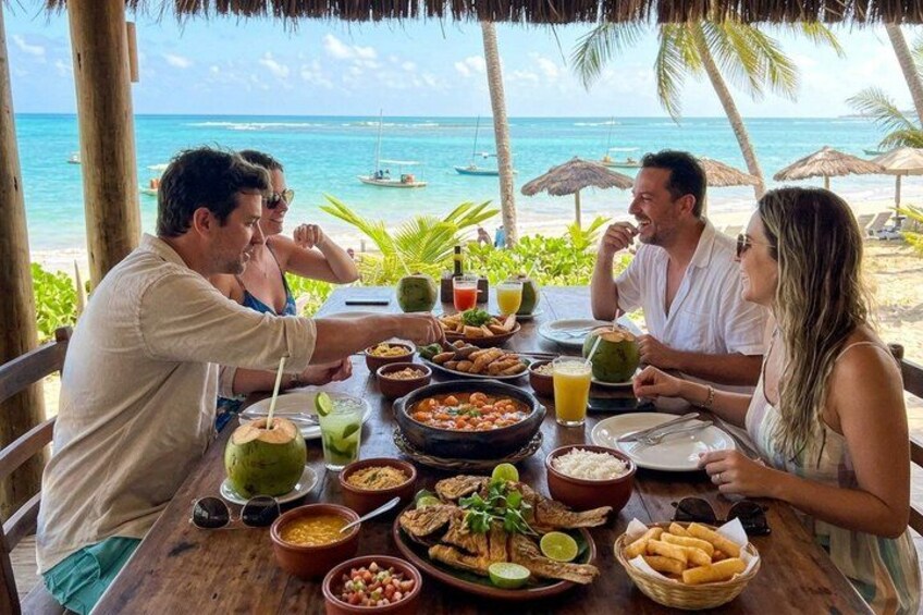 A table with food and drinks on a beach with palm trees and the ocean in the background. 4