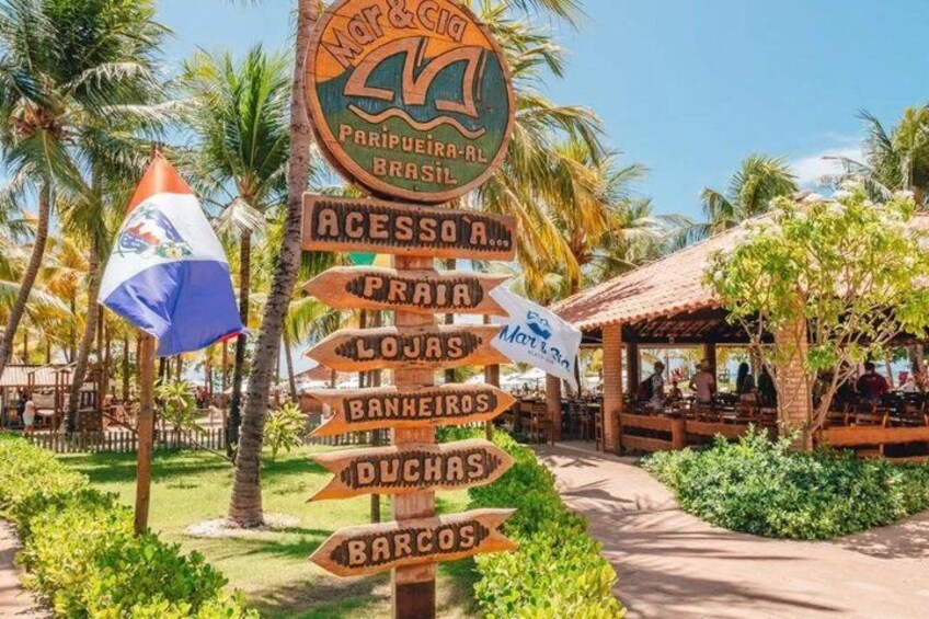 A signpost with multiple directions, palm trees, and a covered outdoor seating area. 5