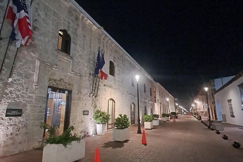 A historic street at night with stone buildings, flags, and street lamps. 4