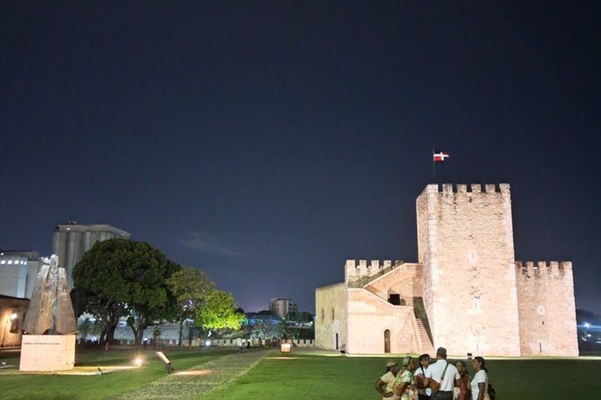 A historic castle with a flag on top, a grassy area, and a statue. 3