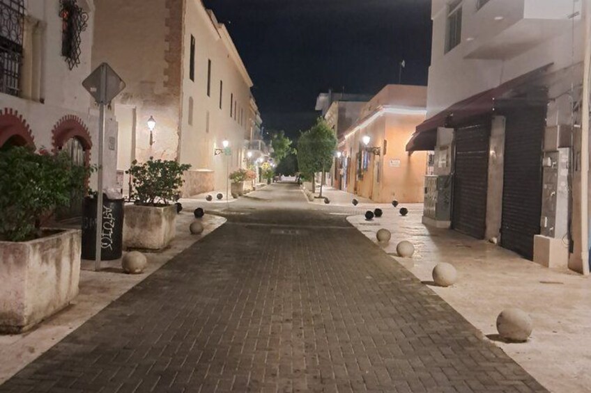 A paved street lined with buildings, some with closed shutters, and decorative bollards along the sidewalk. 2