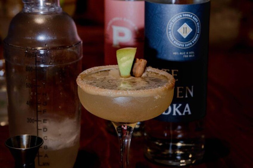 A cocktail with a salted rim, garnished with a slice of lime and a piece of fruit, on a bar counter. 2