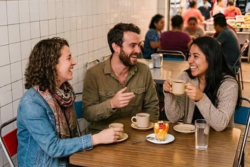 Three people sitting at a table in a cafe, holding cups. 2