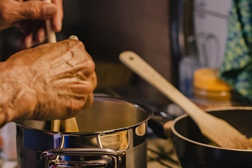 An elderly person's hand stirring a pot on a stove. 1
