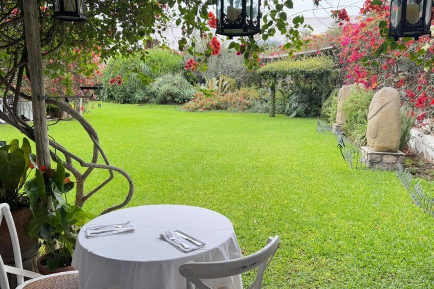 A well-maintained garden with a round table and chairs, surrounded by lush greenery and flowering plants. 2