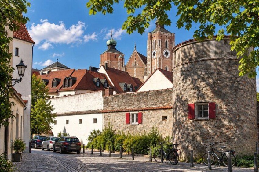 A cobblestone street, historic buildings, a church tower, and a round stone tower. 2