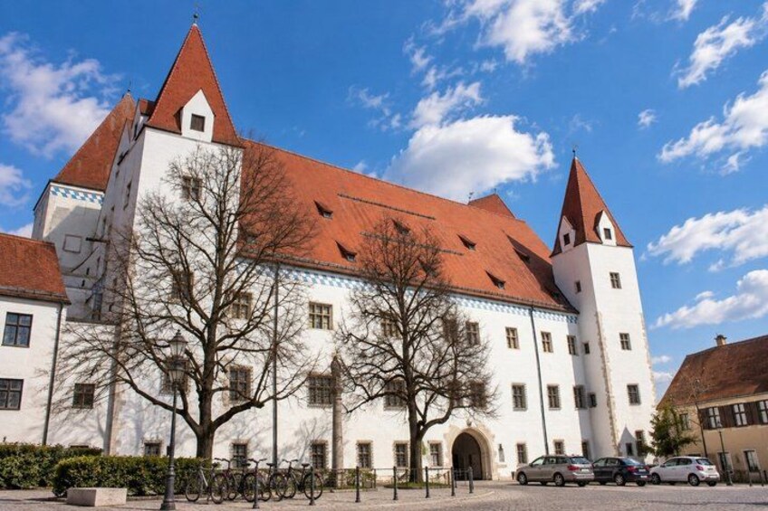 A large white building with a red roof and two towers, surrounded by bare trees and parked cars. 3