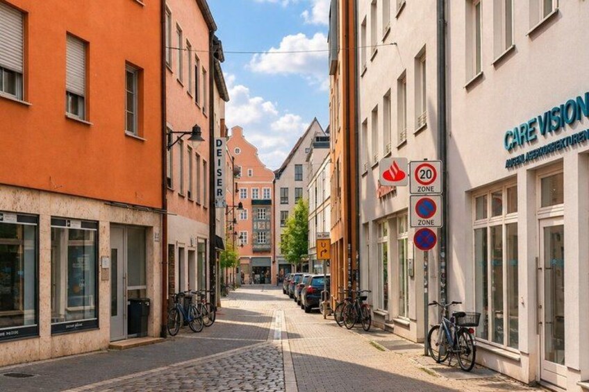 A cobblestone street lined with buildings, including a pharmacy and a care vision clinic. 5