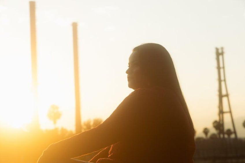 A silhouette of a person against a sunset with industrial structures in the background. 1