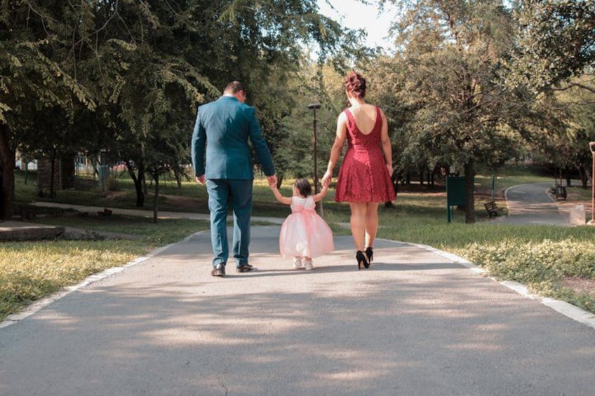 A family walking on a paved path in a park with trees and grass. 3