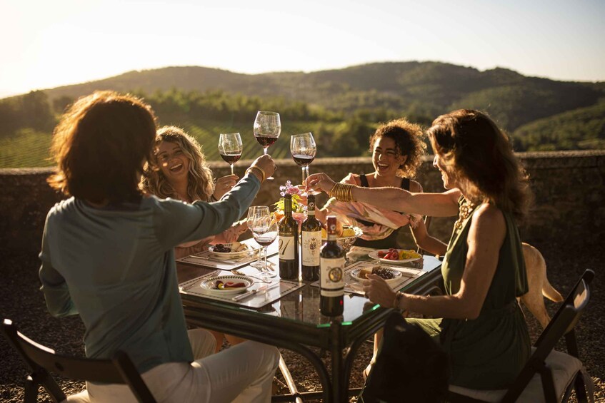 A group of people toasting with wine glasses at a table with a scenic view of hills in the background. 1