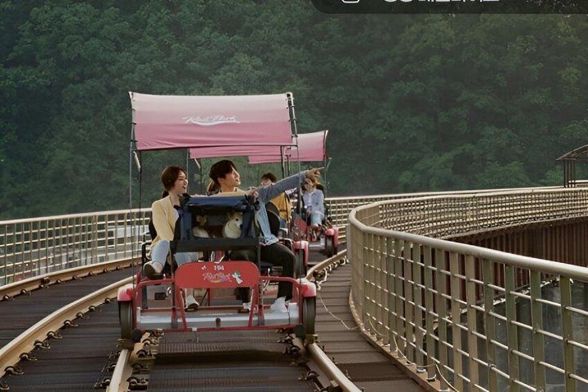 A bridge with a pink canopy, people riding a red vehicle, and a forested background. 4