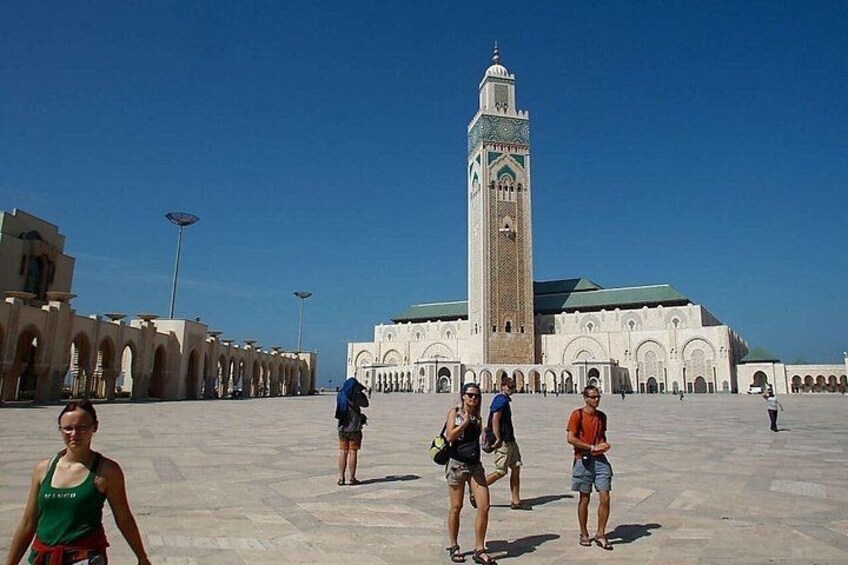 A large open plaza with a tall minaret and arches in the background. 1