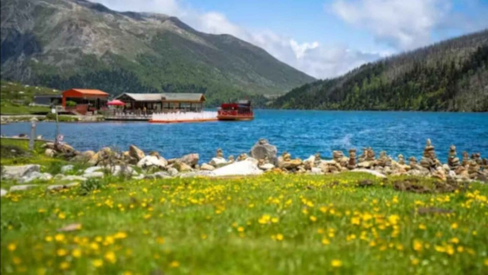 A lake with a boat, a red building, and mountains in the background. 1