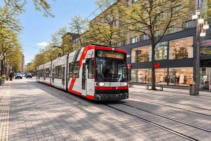 A tram with the number 2 on it, moving along a track with trees and buildings in the background. 3
