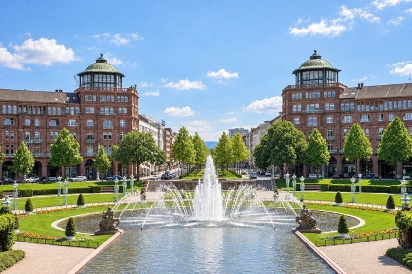 A large fountain in the center of a well-manicured square, surrounded by symmetrical buildings with domed roofs. 5