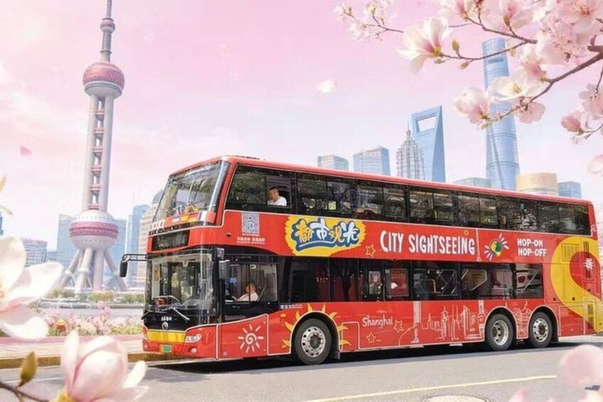 A red double-decker bus with 'City Sightseeing' and 'Shanghai' text, driving past a cityscape with a tower and skyscrapers. 4
